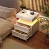 A white nightstand with drawers and LED lighting next to a bed. Podgląd zdjęcia produktu