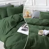 A split image showing a dark green duvet cover and pillowcase set on a bed, with a small lamp and a cup of tea on the right side. Produktbild-Vorschau
