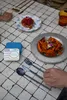 A table setting with food and cutlery, with a hand reaching for the cutlery. Produktbild-Vorschau