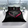 A bed with black bedding featuring a pink heart design with the text "All you need is Love". The bed is set in a room with large windows overlooking a landscape. Produktbild-Vorschau