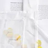 A close-up view of a white sheer fabric with a subtle abstract pattern, overlaid with text from a book or magazine. Slices of lemon are visible on the fabric. Produktbild-Vorschau