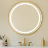 A round, gold-framed LED mirror is mounted on a light beige wall above a white countertop with a marble backsplash. A gold faucet and a gold soap dispenser are visible on the countertop. Podgląd zdjęcia produktu