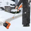 A person is using an electric snow blower to clear snow from a walkway in front of a house. Podgląd zdjęcia produktu