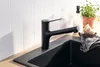 A black kitchen faucet is shown in a modern kitchen setting, with white subway tiles in the background and a black sink. Produktbild-Vorschau