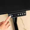 A close-up of a person's finger pressing a button on a black desk control panel. Produktbild-Vorschau