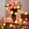 A bouquet of artificial roses with integrated LED lights, arranged in a vase on a table, with a string of rose lights draped around. Produktbild-Vorschau
