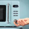 A close-up shot of a light blue retro-style microwave with a hand turning a dial. Podgląd zdjęcia produktu