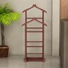 A wooden valet stand is shown in a room with a potted plant and a piece of furniture in the background. Produktbild-Vorschau