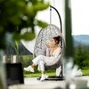 A woman is sitting in a hanging chair outdoors, drinking from a glass. Náhled obrázku produktu