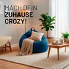 A cozy living room scene with a blue beanbag chair, a blanket, a pillow, a plant, and a coffee table. Voir les images du produit