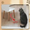 A cat is looking at a toy snake on the floor next to a small white chair. Náhled obrázku produktu