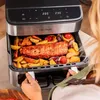 A person is pulling out a tray from an air fryer filled with food. Produktbild-Vorschau
