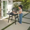 A woman is using an electric grill on a patio. Voir les images du produit