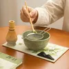 A person is preparing matcha tea, sifting green tea powder into a bowl. Produktbild-Vorschau