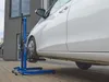 A white car is being lifted by a blue car jack. Produktbild-Vorschau