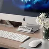 A Satechi USB-C Combo hub is placed on a desk in front of an Apple iMac computer, with a keyboard and mouse also visible. A vase of white flowers is to the right of the computer. Náhled obrázku produktu