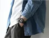 A person wearing a denim shirt and a white t-shirt, with a watch on their wrist. Voir les images du produit