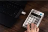 A hand is typing on a white retro-style number pad connected to a black laptop via a USB drive. Produktbild-Vorschau
