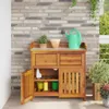 A wooden garden cabinet with drawers and a cupboard, placed on a patio in front of a brick wall. Produktbild-Vorschau