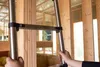 A close-up view of a person's hands holding a section of a silver telescopic ladder. The ladder is positioned against a wooden wall frame of a building under construction. Produktbild-Vorschau