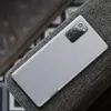 The back of a Samsung Galaxy Note 20 phone with a textured gray fabric case, resting on a dark gray textured surface. Produktbild-Vorschau