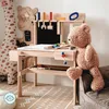 A child's wooden workbench with tools and accessories, a teddy bear sitting on a couch next to it, and a giraffe plush toy in the background. Náhled obrázku produktu