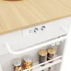A close-up view of a white kitchen cart with a wooden countertop, featuring built-in electrical outlets and a towel bar. Several glass jars filled with food items are visible on the shelves below. Produktbild-Vorschau