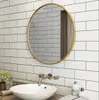 A round gold-framed mirror is mounted on a white subway tile wall above a white sink and faucet in a bathroom. Podgląd zdjęcia produktu