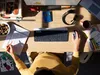 A person's hands are visible working at a desk with a keyboard, mouse, calculator, and notebook. The scene is lit by sunlight casting shadows. Anteprima dell’immagine prodotto