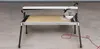 A tile saw is set up on a concrete floor, with a tile on its cutting surface. Anteprima dell’immagine prodotto
