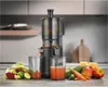 A juicer is shown on a kitchen counter with fruits and vegetables. Podgląd zdjęcia produktu
