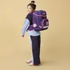 A young girl wearing a backpack and standing against a plain background. Produktbild-Vorschau