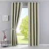A room interior with a window covered by beige curtains. A small table with decorative items is placed to the left of the window. Produktbild-Vorschau