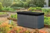 A garden storage box sits in a garden with raised beds of plants. Voir les images du produit