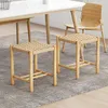 Two wooden stools with woven seats are placed on a grey rug in front of a dining table. A wooden chair is visible in the background. Podgląd zdjęcia produktu