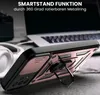 A close-up of a rose gold and black phone case with a ring stand, placed on a wooden surface with a laptop and headphones in the background. Produktbild-Vorschau