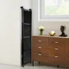 A black folding shelf unit is shown standing next to a wall, with a dresser and window in the background. Voir les images du produit