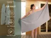 A woman is holding a large gray towel in a sauna-like environment, with text overlays describing the towel's features. Produktbild-Vorschau