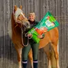 A woman stands next to a horse, holding a large bag of horse feed. Anteprima dell’immagine prodotto
