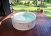An inflatable hot tub is situated on a wooden deck, with a lush green lawn and trees in the background. Náhled obrázku produktu