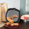 A hand holding a red silicone handle attached to a cast iron grill pan with ribs inside, placed on a wooden cutting board. Voir les images du produit