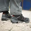 Close-up of a person's feet wearing black safety shoes on a gravel surface. Produktbild-Vorschau