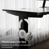 A white headphone is hanging from a black hook attached to the underside of a black desk. The background is a blurred white curtain. Produktbild-Vorschau