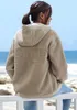 A woman is sitting on a white railing, looking out at the ocean. She is wearing a fleece jacket. Produktbild-Vorschau