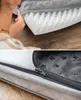 A person's hand is shown touching the foam interior of a gray pet bed. The bottom half of the image shows a close-up of the zipper and the paw print pattern on the inside lining of the pet bed. Produktbild-Vorschau