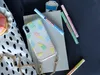 A flat lay of stationery and accessories, including markers, a phone case, cookies, and a notebook. Produktbild-Vorschau