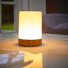 A bedside table lamp with USB charging ports sits on a reflective surface, with a window and sofa visible in the background. Produktbild-Vorschau