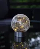 A solar-powered decorative light with a cracked glass sphere and LED lights, placed on a reflective surface. Produktbild-Vorschau