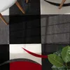 A close-up view of a rug with a geometric pattern, featuring a plant in the foreground. Produktbild-Vorschau
