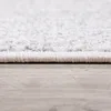 A close-up, side view of the edge of a rug on a wooden floor. Produktbild-Vorschau